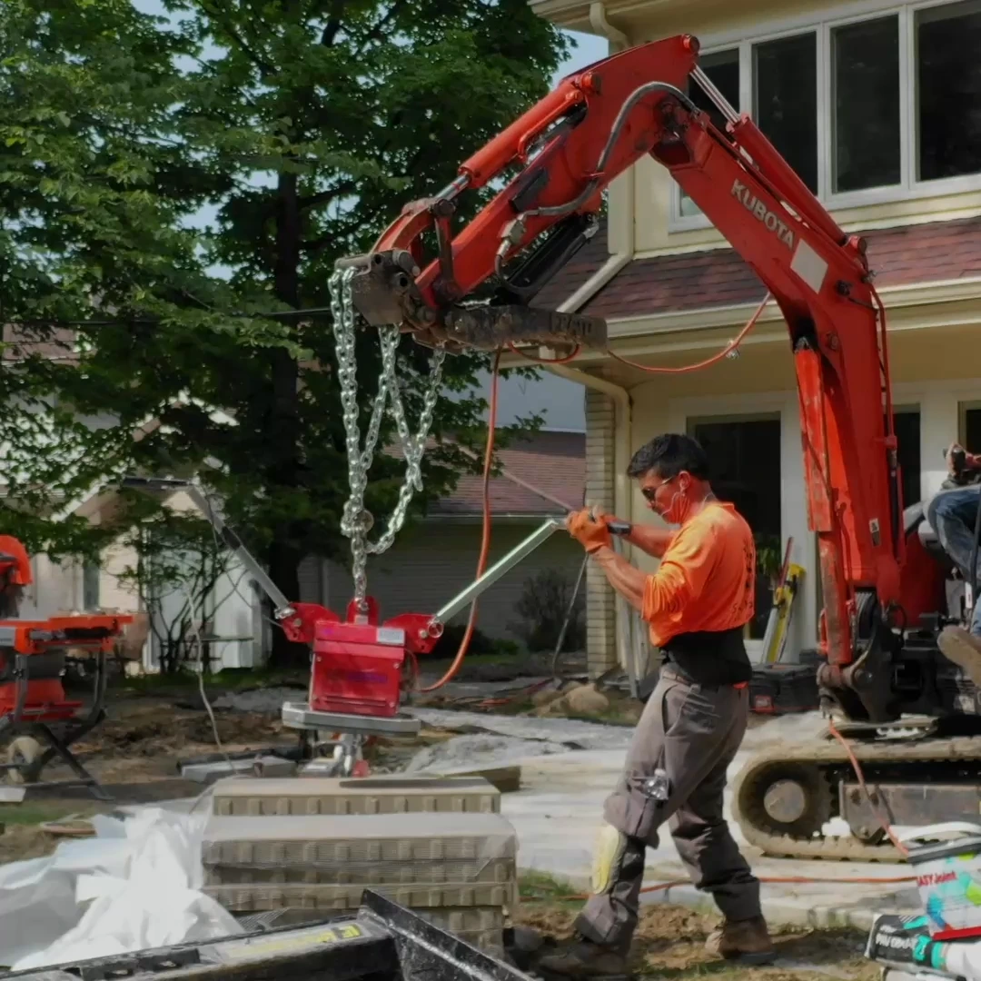 Mini excavator lifting a paver slab into place with a vacuum lifter