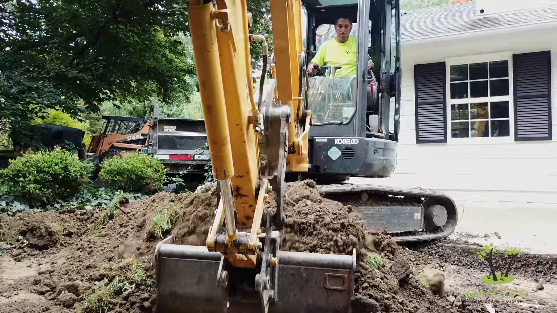 Tracked excavator cutting into a front yard beside the house